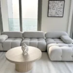 TUKA Dubai Cozy Cloud living room furniture package installed in a Downtown Dubai high-rise, featuring an off-white modular tufted sofa, fluted wood coffee table, and monochrome abstract wall art.